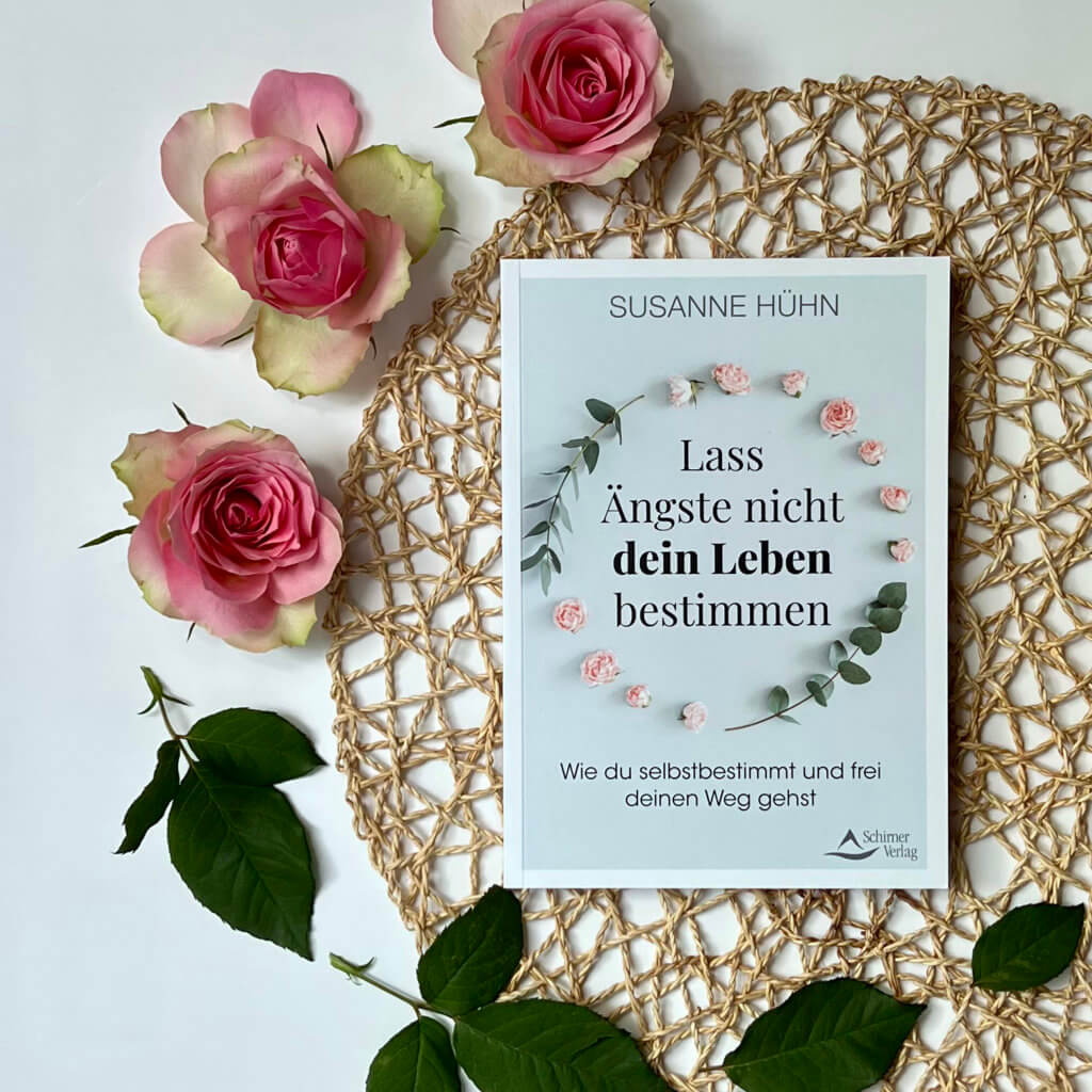 Das Bild zeigt das Buch "Lass Ängste nicht dein Leben bestimmen" von Susanne Hühn auf einem hellblauen Hintergrund umgeben von Rosen.