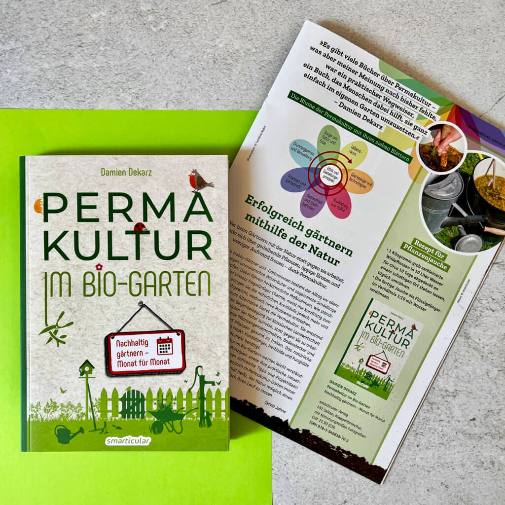 Das Bild zeigt das Buch "Permakultur im Bio-Garten" von Damien Dekarz aus dem smarticular Verlag auf grauem Hintergrund neben einer Zeitschrift.