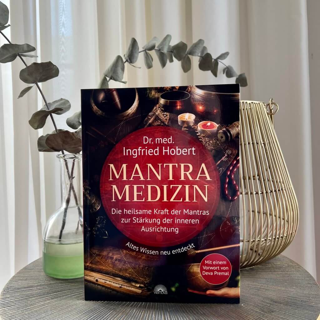 Das Bild zeigt das Buch Mantra Medizin von Ingfried Hobert stehen auf einem Tisch.